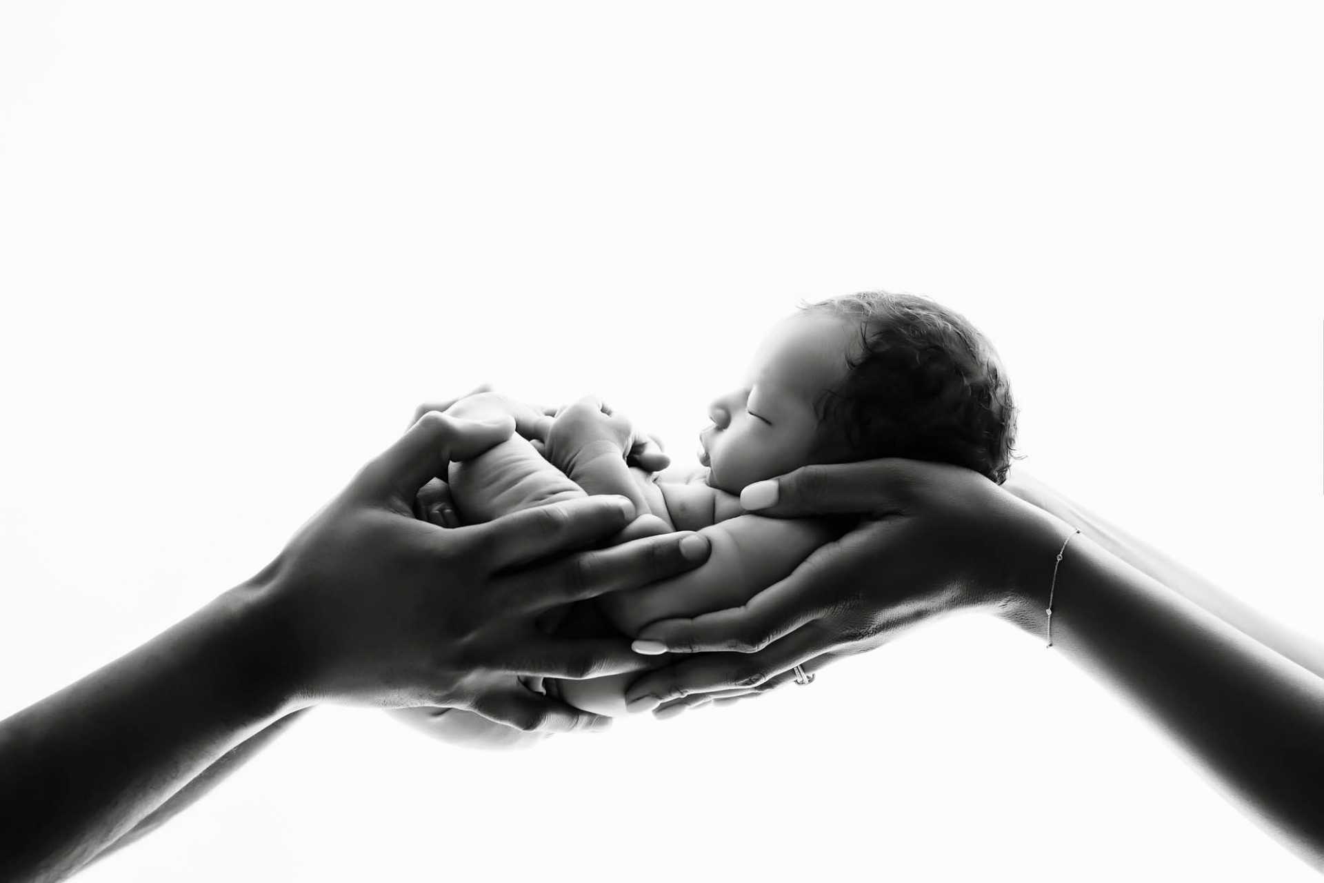 Dallas Newborn Photographer | Timeless Black & White Newborn Portrait Black and white newborn portrait of baby held gently in parents’ hands – Dallas newborn photographer