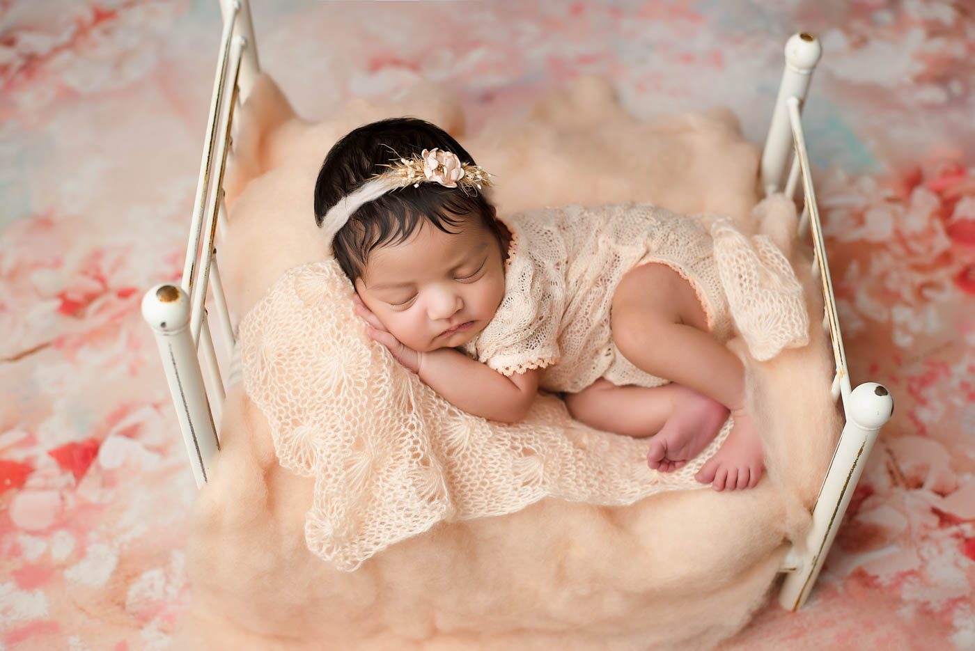 Newborn Posed On A Miniature Bed Surrounded By Soft Newborn Photography Props
