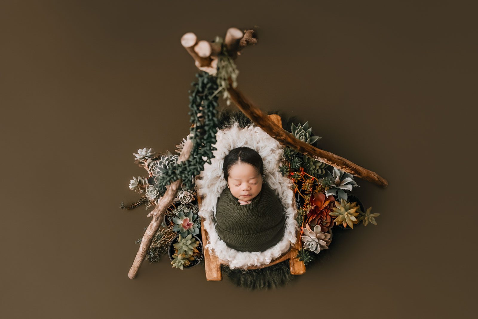 Newborn Baby Wrapped In Green Fabric During A Professionally Styled Portrait Session