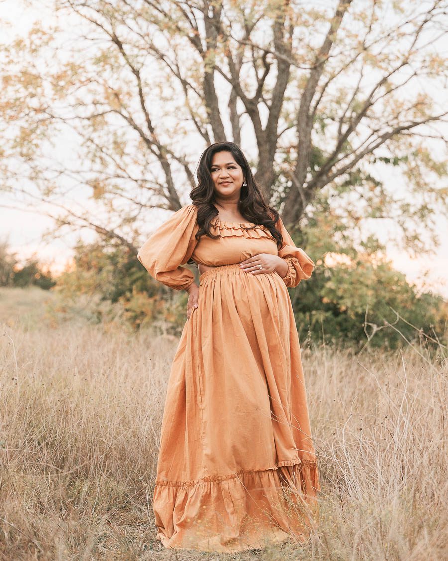 Expecting Mother Standing In Tall Grass During An Outdoor Maternity Portrait Session With Neutral Styling.