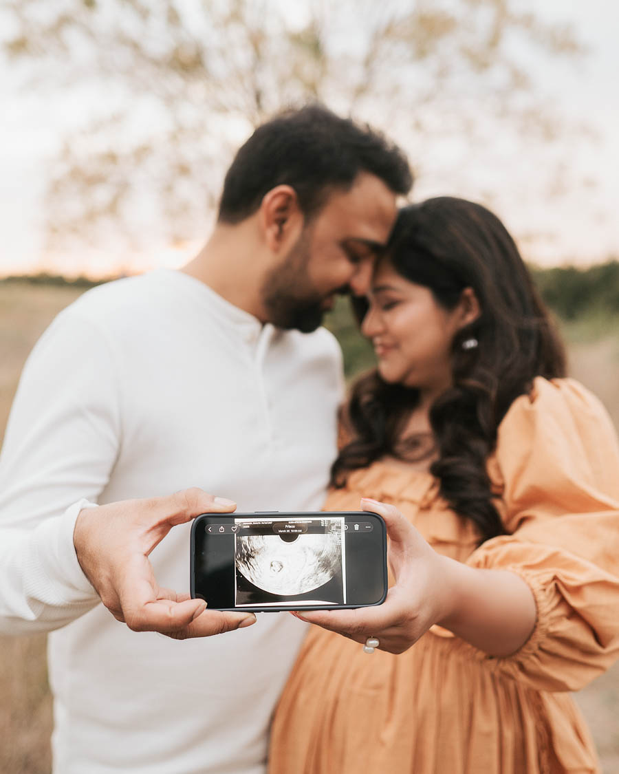 Expecting Couple Holding Ultrasound Photo During An Outdoor Maternity Portrait Session.
