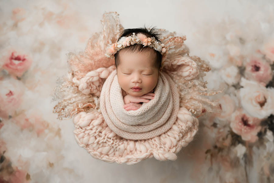 Sleeping Newborn Baby Wrapped In Soft Neutral Fabric During A Calm Newborn Portrait Session With Delicate Floral Styling.