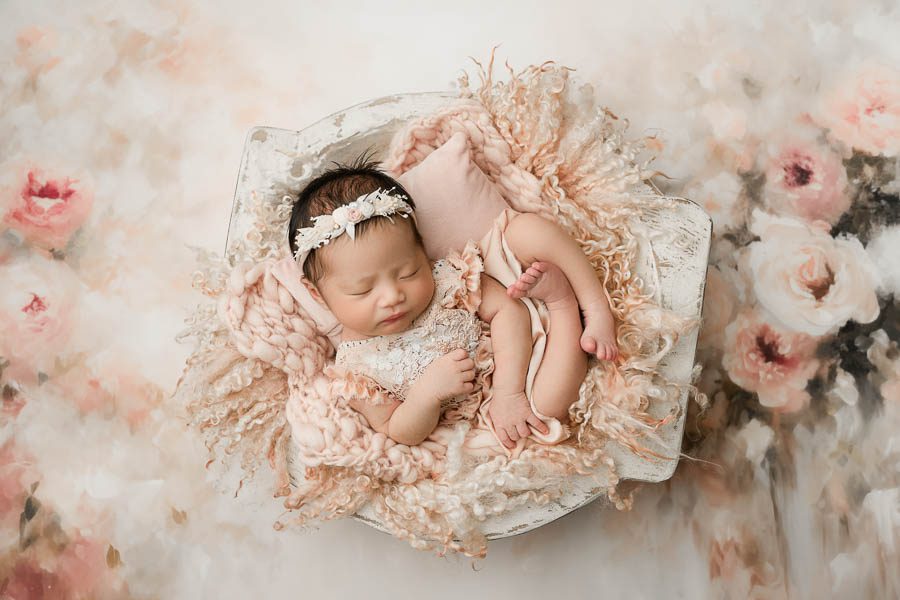 Sleeping Newborn Baby Posed In A Soft Floral Newborn Setup With Delicate Neutral Textures And Blush Tones.