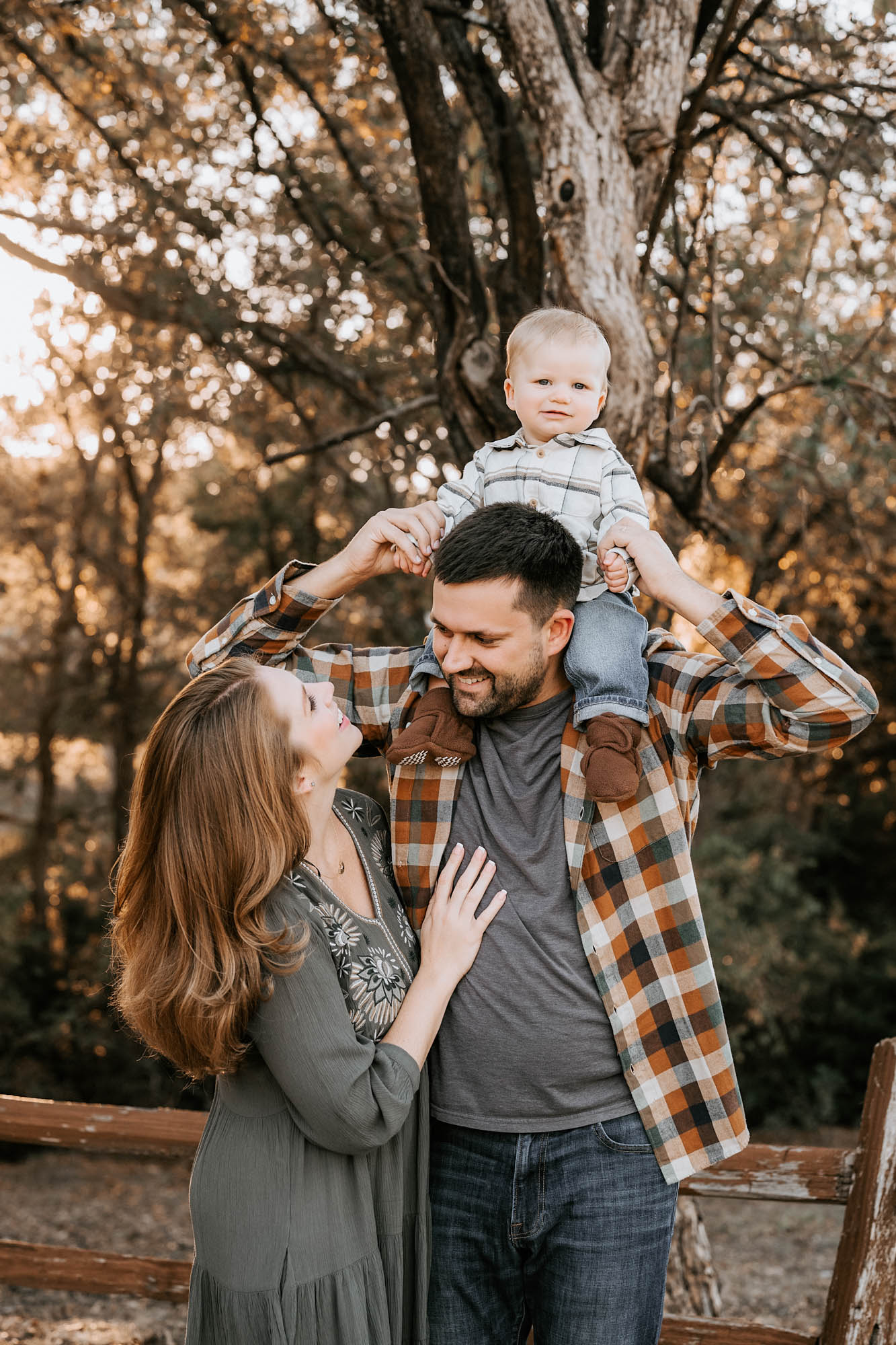 Smiling parents with baby boy on dad’s shoulders during an outdoor family photography session in Dallas
