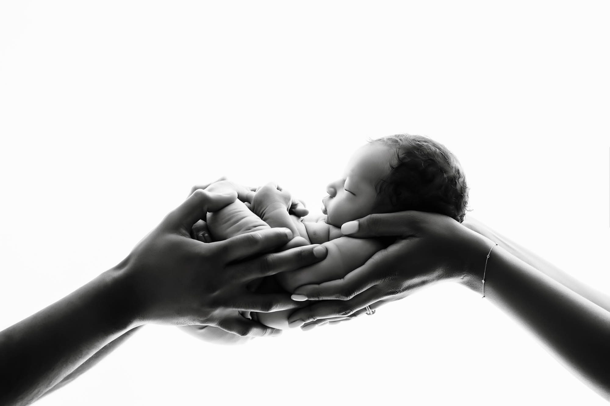Black and white newborn portrait of baby held gently in parents’ hands – Dallas newborn photographer