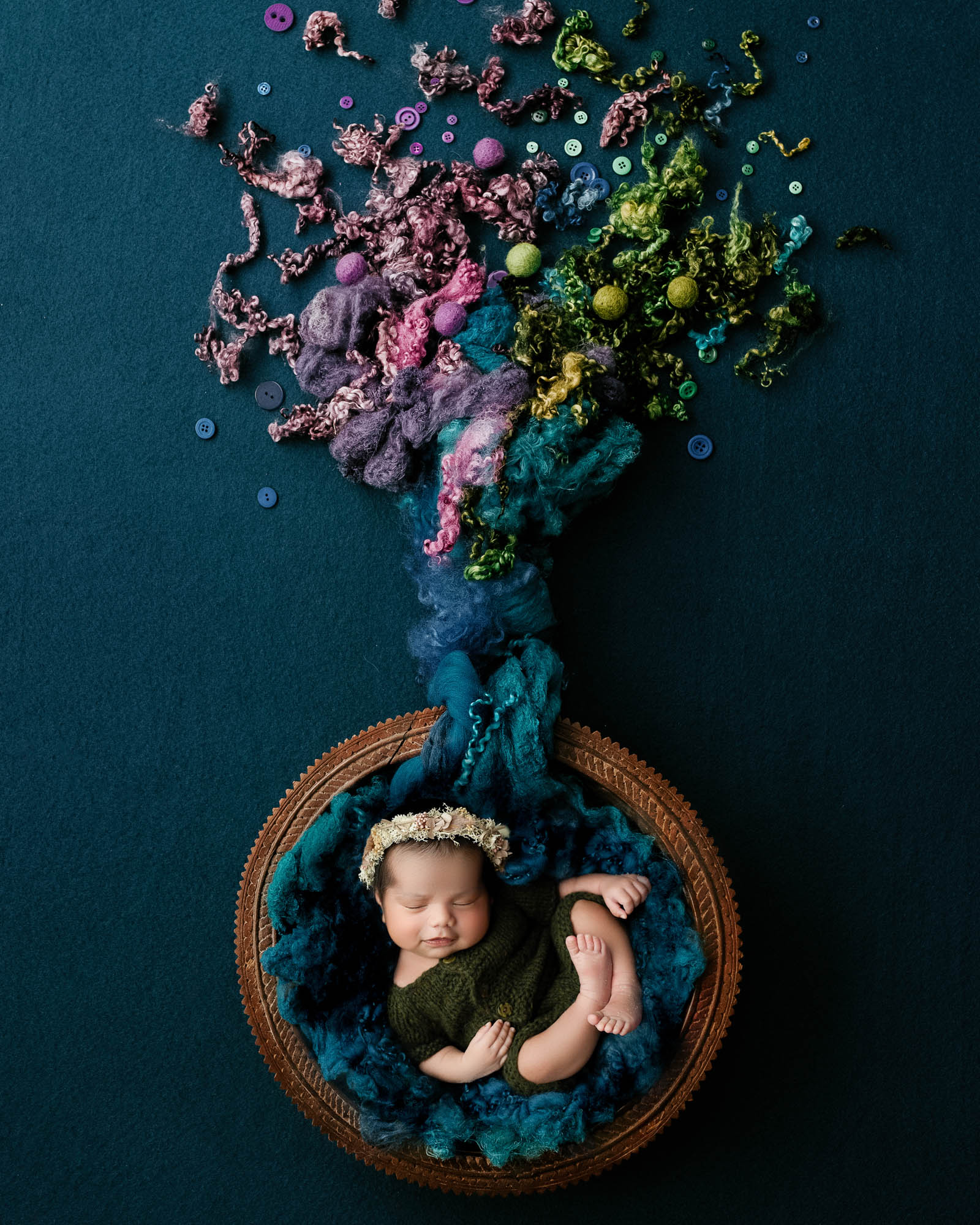 Newborn baby peacefully sleeping in a styled basket setup with colorful textures and a floral headband, photographed by Dallas newborn photographer Lily Hayes Photography.