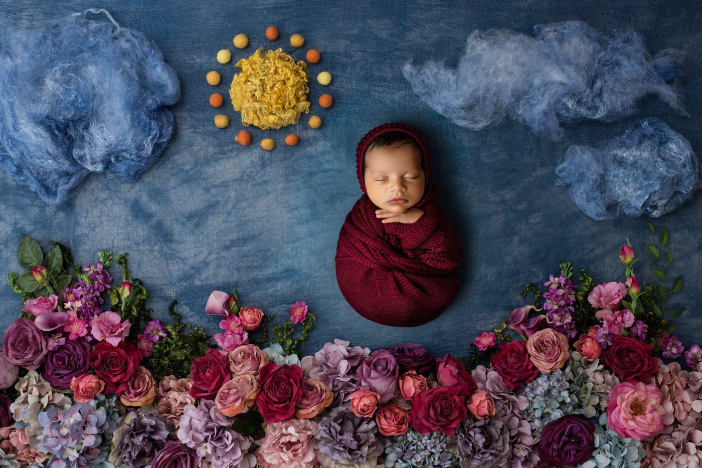 Artistic Newborn Photo With Vibrant Florals And Deep Red Wrap Styling