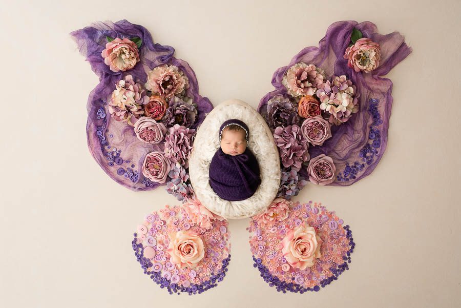 Newborn baby posed in a butterfly-inspired floral portrait setup