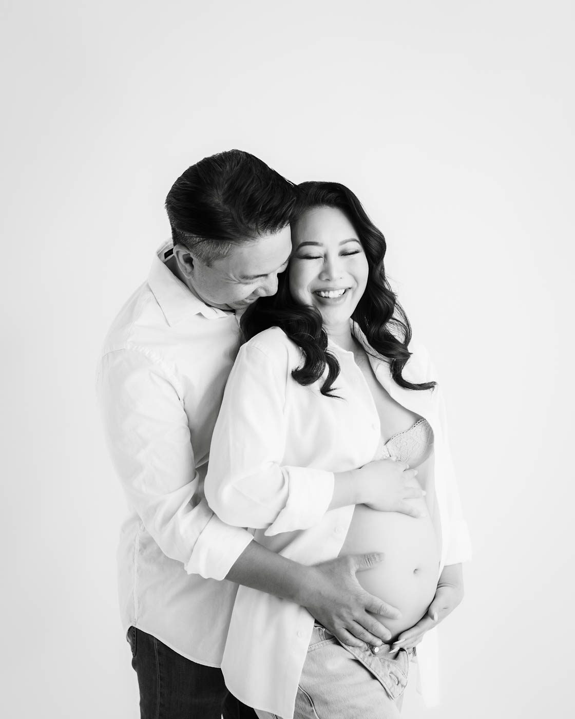 Expecting Couple Embracing During Black-And-White Studio Maternity Photography Session