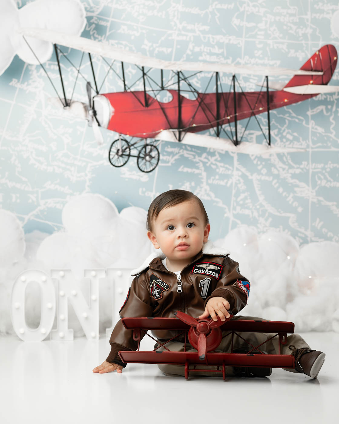 One-Year-Old Boy Posing With A Vintage Airplane Backdrop During A First Birthday Portrait Session In Dallas