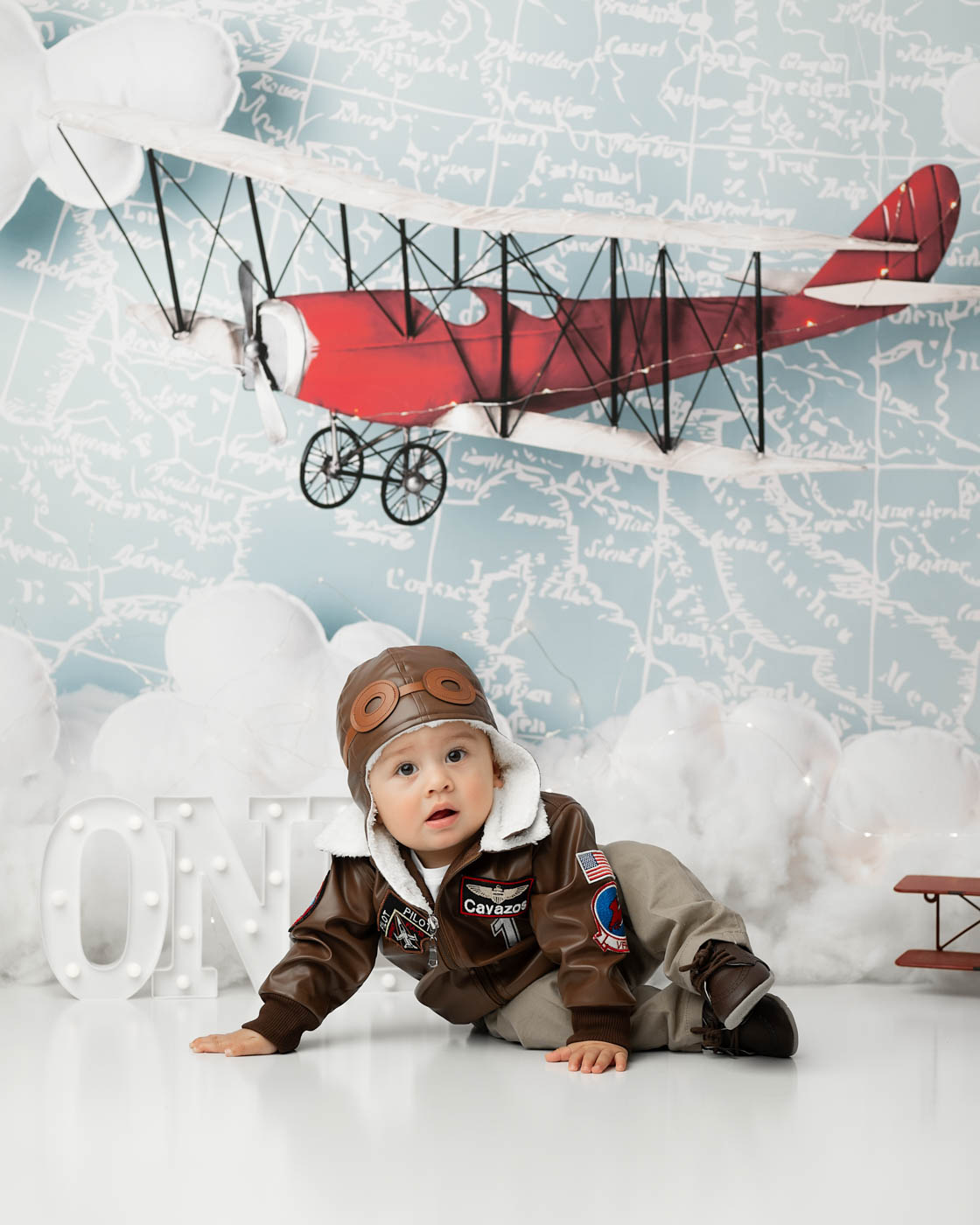 Baby Boy Dressed In An Aviator Outfit For A Vintage Airplane First Birthday Photography Session