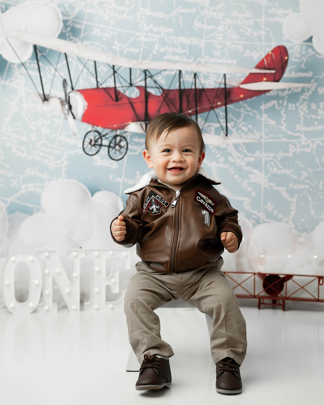 Standing One-Year-Old During A Baby First Birthday Photography Session With A Vintage Airplane Backdrop