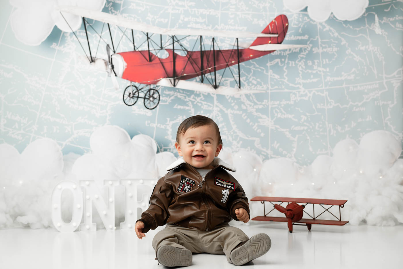 Happy One-Year-Old Sitting Beneath A Vintage Airplane During A Dallas First Birthday Portrait Session