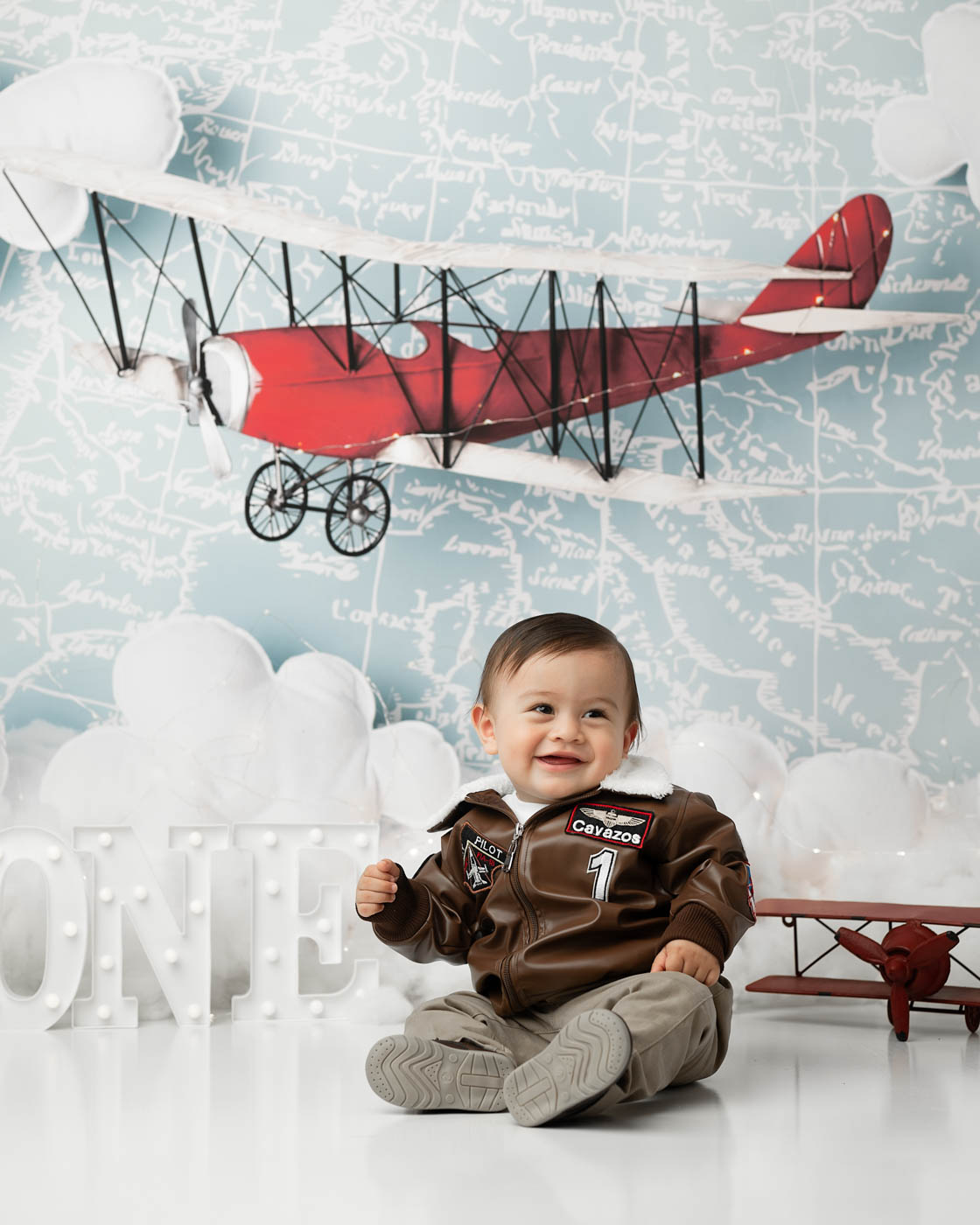 One-Year-Old Boy Smiling Beside A Vintage Airplane Prop During A Dallas Portrait Session