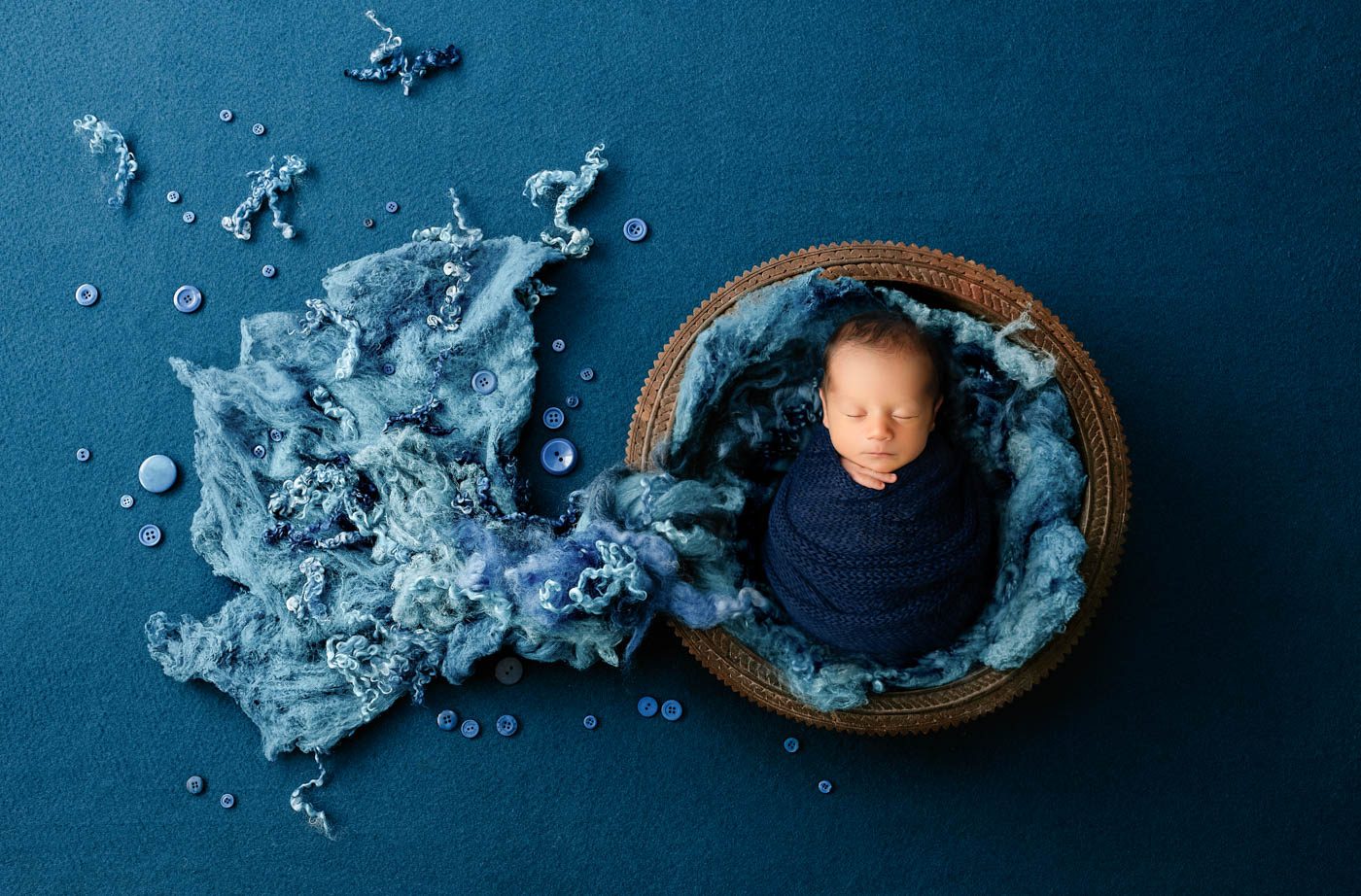 Wrapped Newborn Posed Inside A Handcrafted Wooden Basket With Layered Blue Textures During A Dallas Newborn Photography Session.