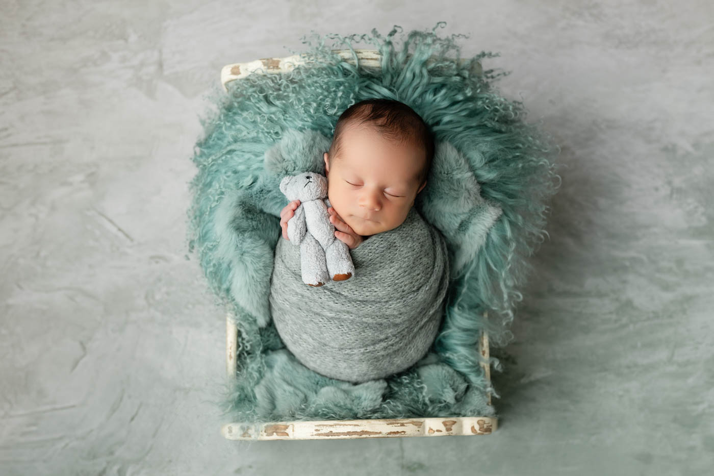 Overhead Newborn Portrait Of A Sleeping Baby Wrapped In Soft Aqua Layers During A Newborn Portrait Session In Dallas.