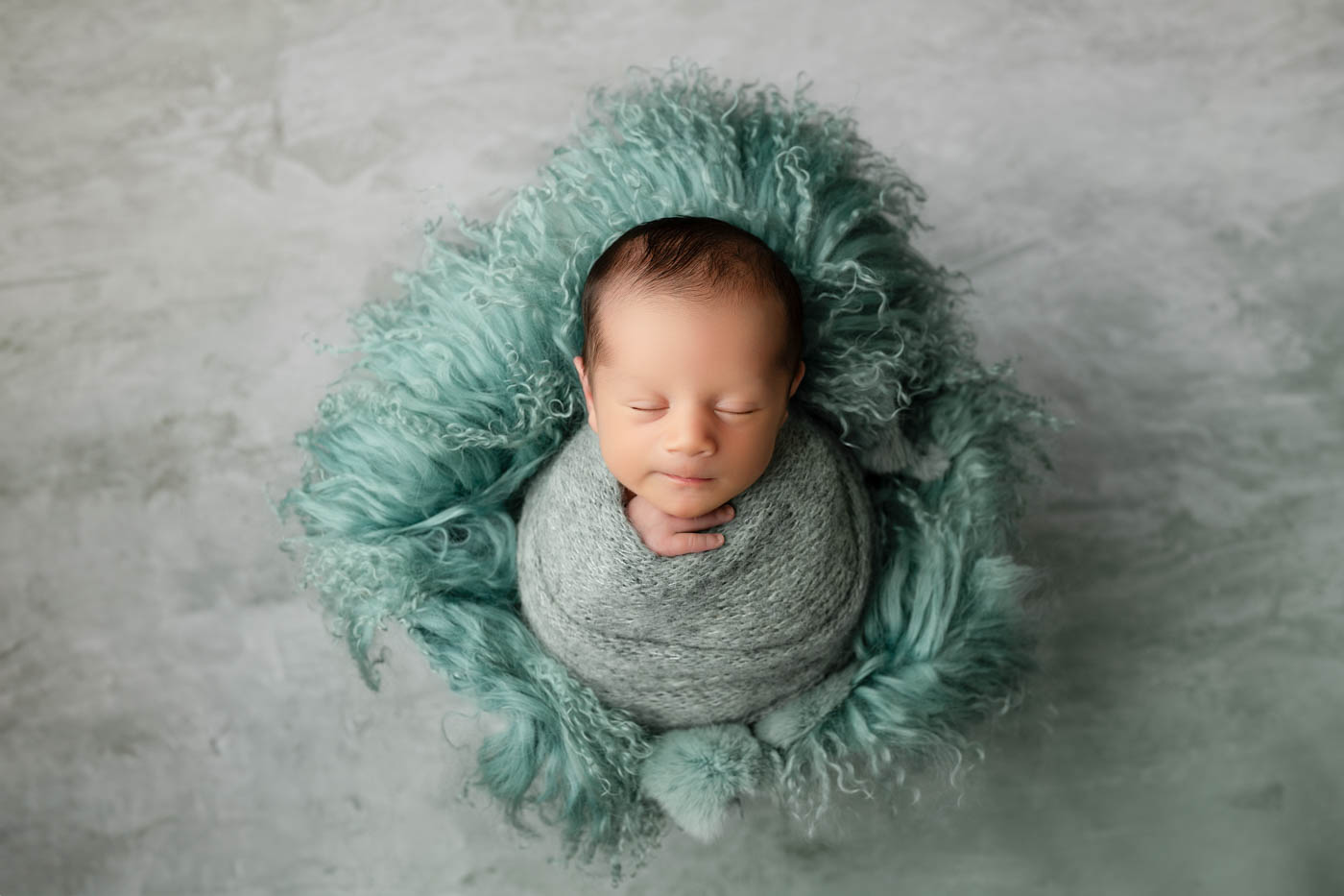 Professional Newborn Portraits In Dallas Featuring A Wrapped Baby Resting On Textured Aqua Faux Fur.