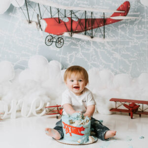 Baby boy celebrating his first birthday with an airplane-themed cake smash photography session in Dallas, featured alongside a five-star client review.