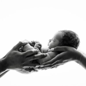 Black and white newborn portrait of a sleeping baby held in parents' hands during a Dallas newborn photography session, featured with a five-star client review.