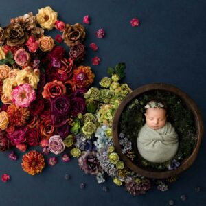 Fine art newborn portrait of a sleeping baby wrapped in a wooden bowl surrounded by colorful floral arrangements during a Dallas studio newborn photography session, featured with a five-star client review.