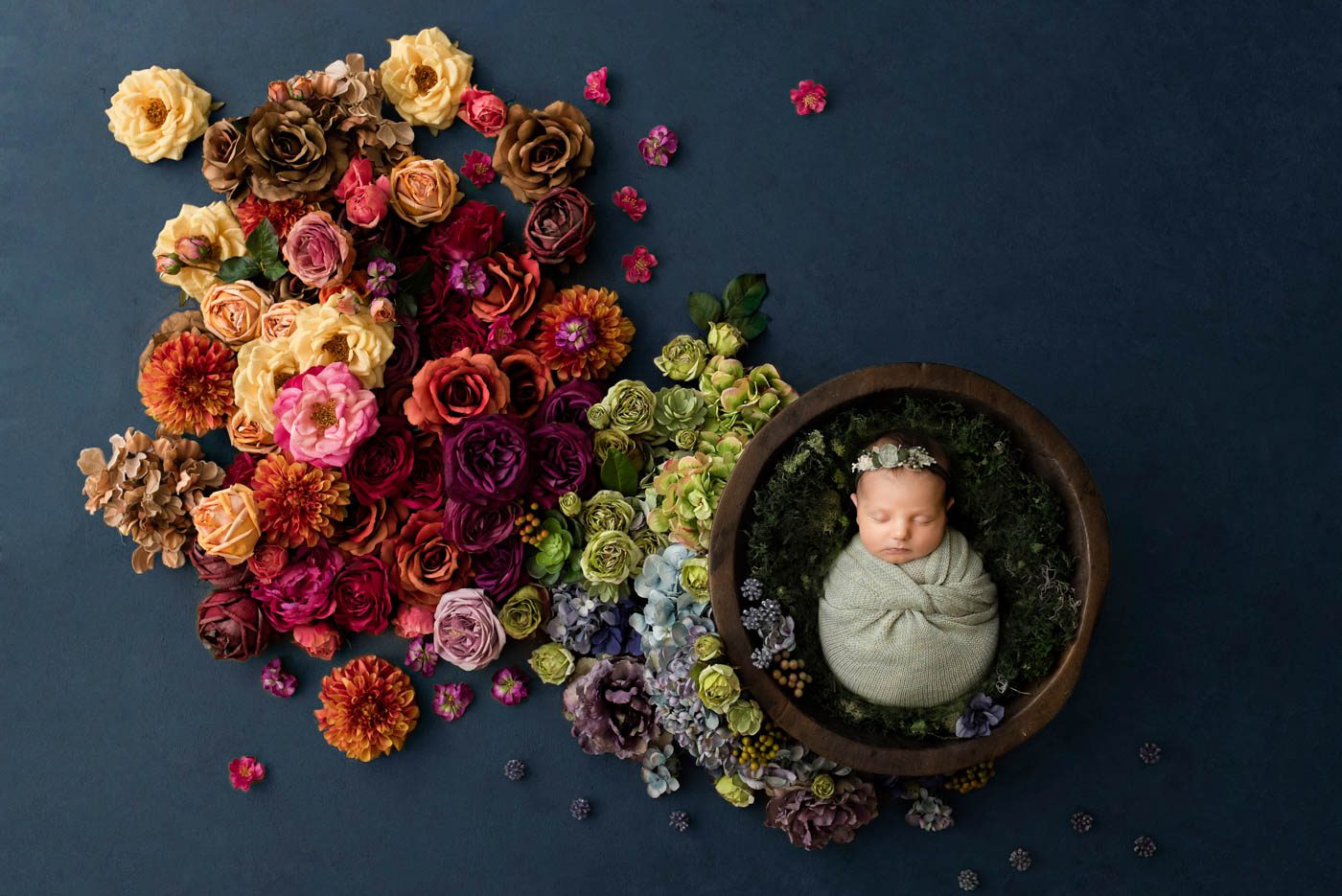 Fine art newborn portrait of a sleeping baby wrapped in a wooden bowl surrounded by colorful floral arrangements during a Dallas studio newborn photography session, featured with a five-star client review.