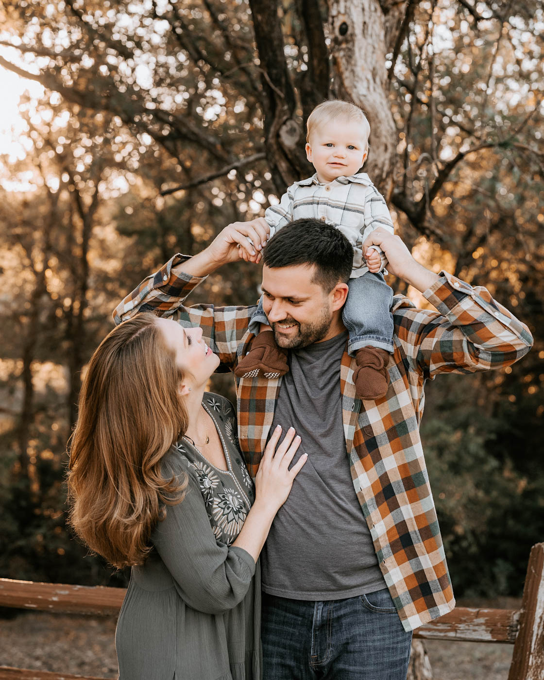Family of three enjoying an outdoor fall family photography session in Dallas with their toddler on dad's shoulders during golden evening light.
