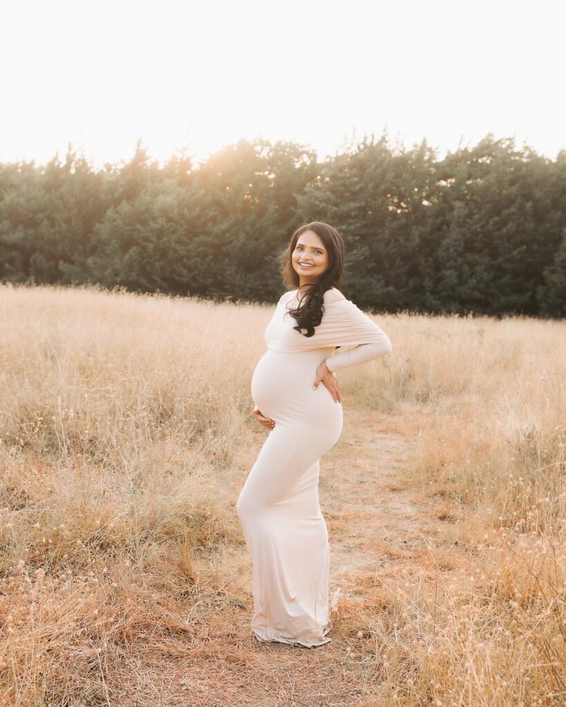 Outdoor Maternity Photography In Dallas With Expecting Mother Posed In Profile Wearing A Fitted Neutral Maternity Gown.