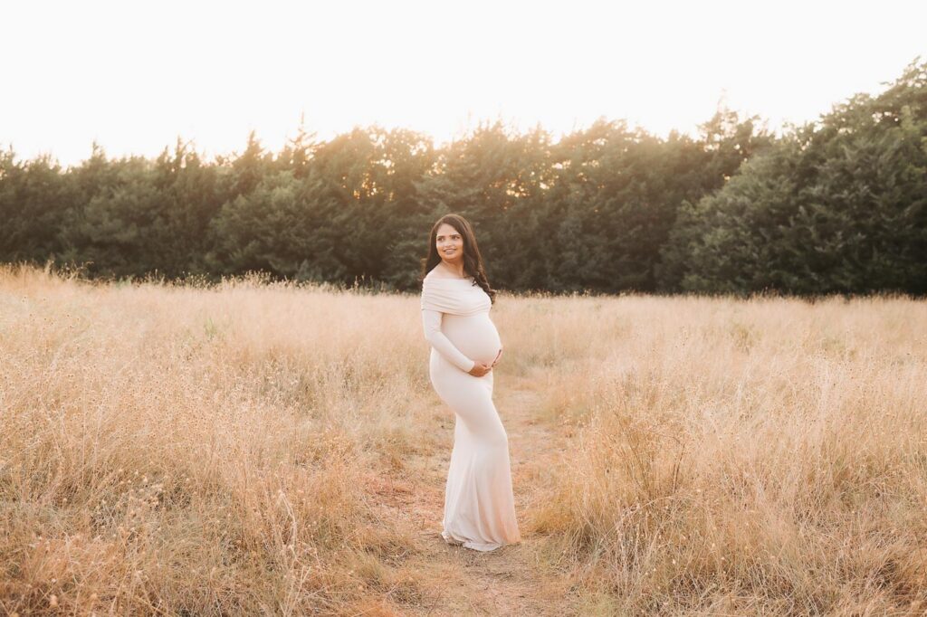 Wide Outdoor Maternity Portrait In Dallas Showing Expecting Mother Standing In A Natural Field Setting.