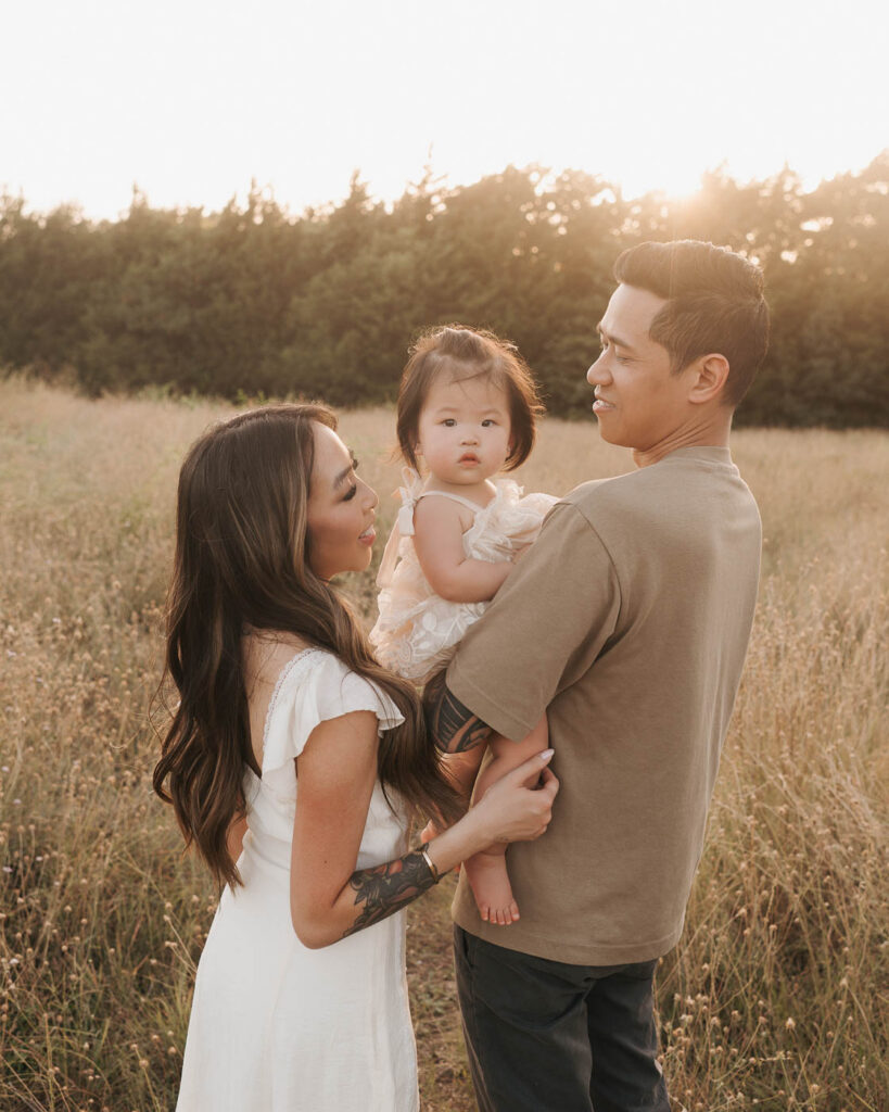What If My Child Won’t Cooperate During Family Photos? 7 Dallas Family Photography Session With Parents Interacting With Their Toddler While Dad Holds Her Outdoors.