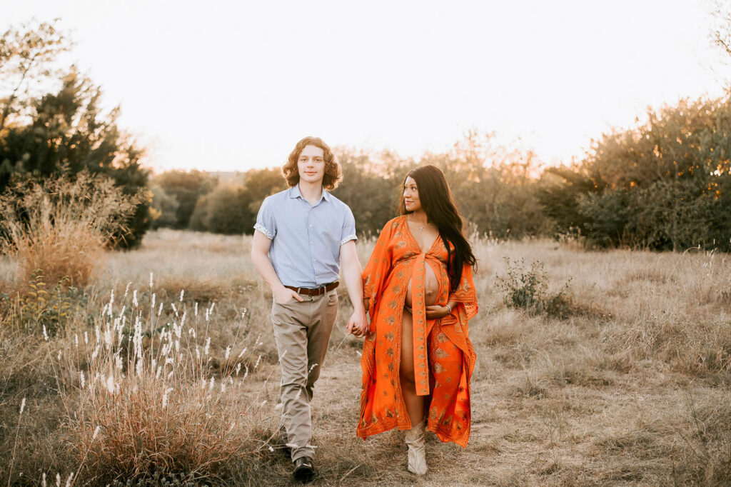 Should Your Partner Be Included In Your Maternity Photos? 5 Pregnancy Photographer Dallas Portrait Of Expecting Mother In An Orange Gown Walking Outdoors With Her Partner