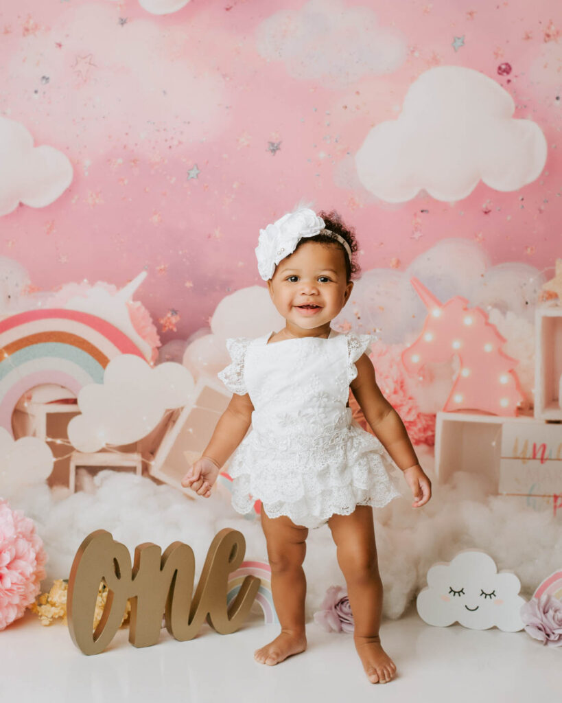 Baby Girl Standing In A Pink Rainbow Cake Smash Photography Setup In Dallas