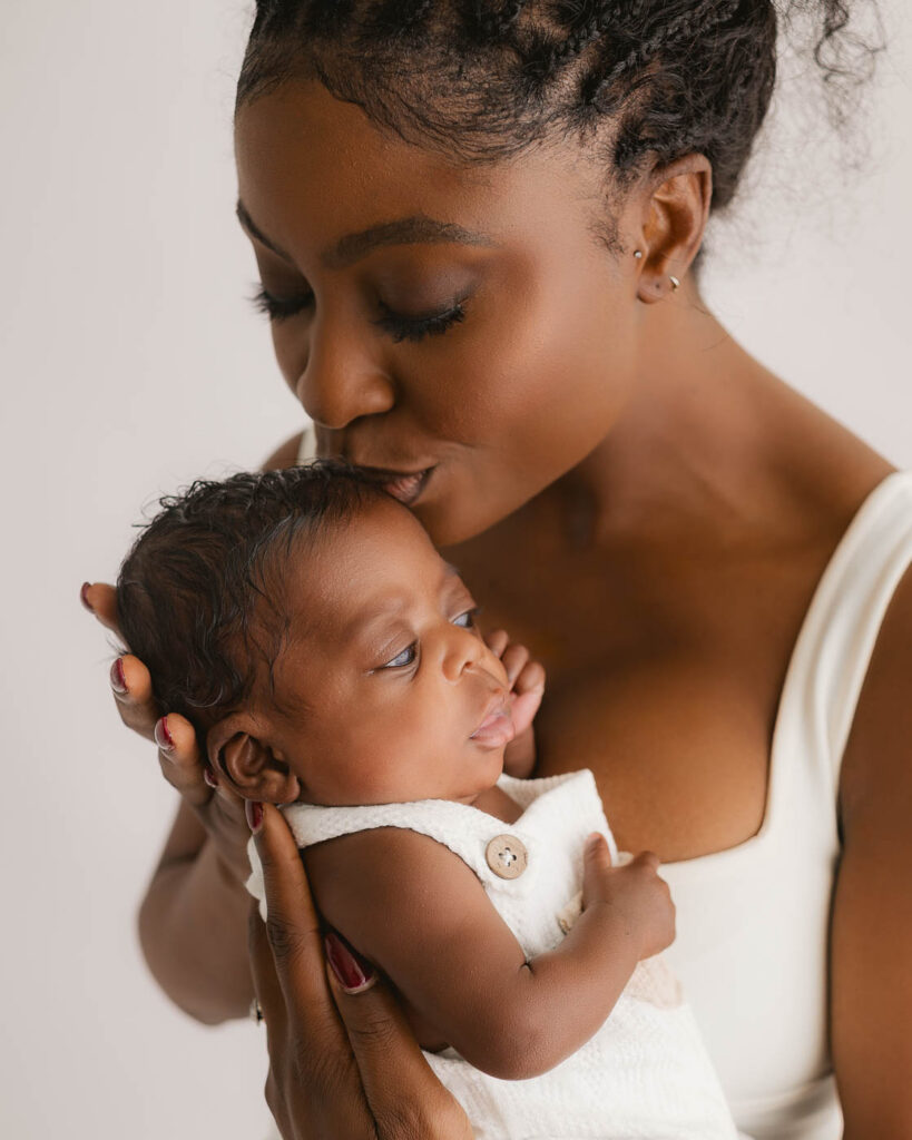 Mother Holding And Kissing Her Newborn During A Dallas Newborn Photography Session
