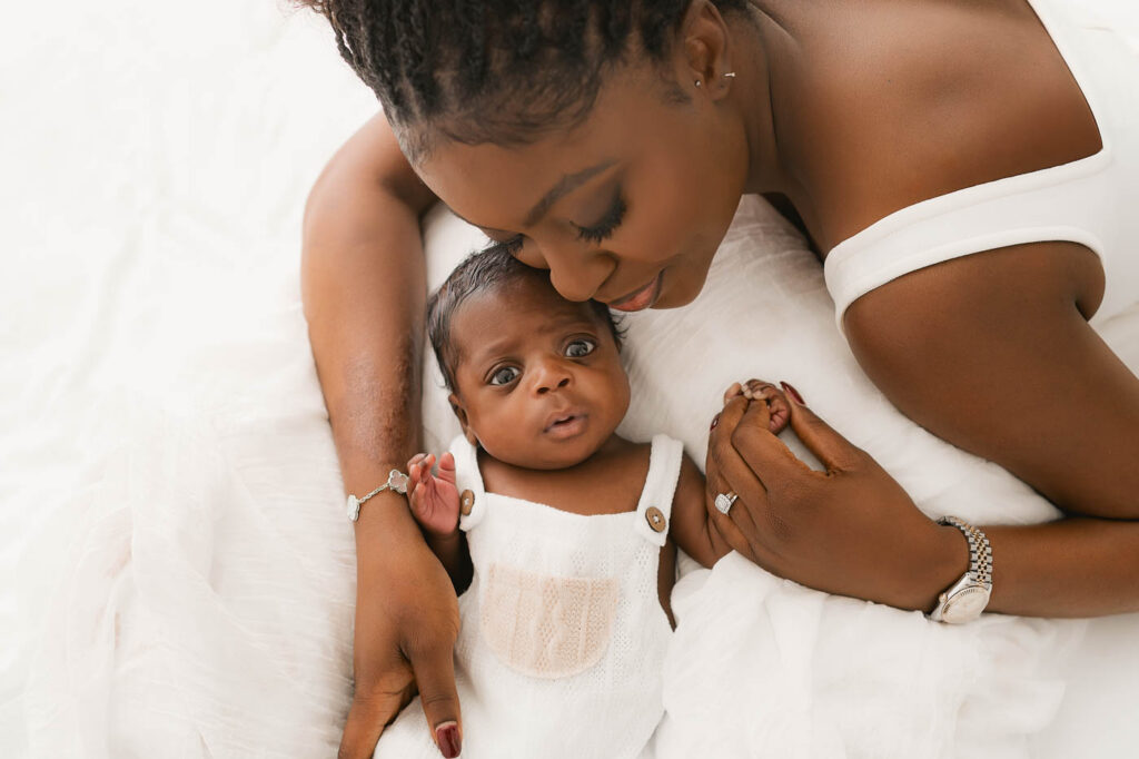 Mother Kissing Her Newborn During A Dallas Newborn Photography Session With Simple White Clothing