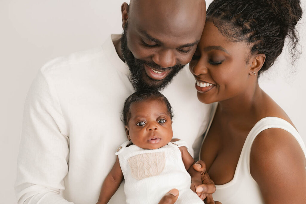 Parents Smiling While Holding Their Newborn During A Studio Newborn Session In Dallas