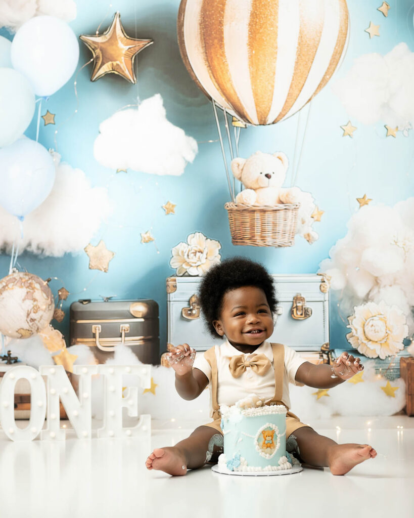 Smiling Baby Sitting With His First Birthday Cake During A Cake Smash Session In Dallas.