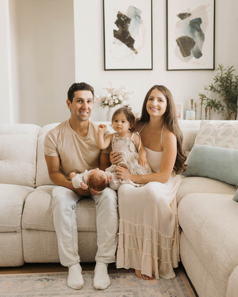 Dallas Newborn Photographer Capturing Parents With Their Newborn Son And Older Daughter Sitting Together On A Neutral Studio Sofa