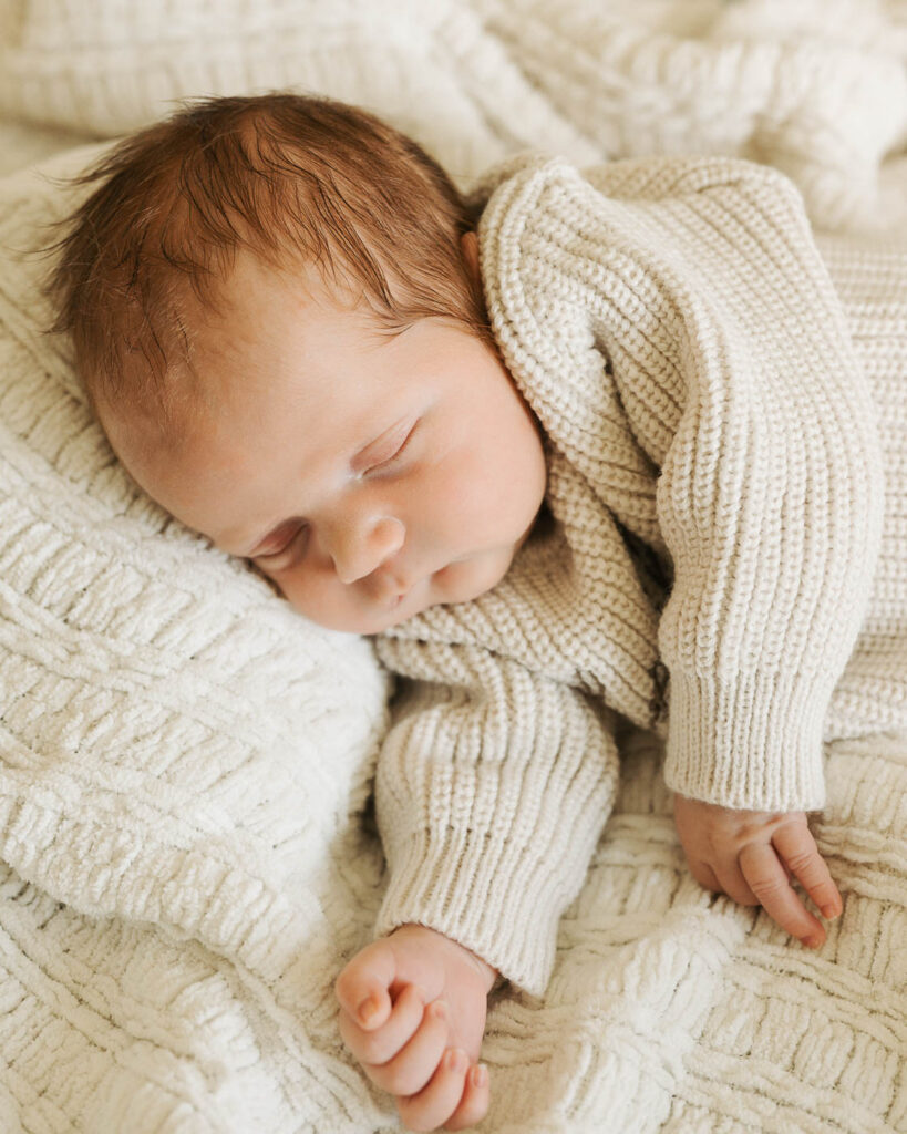 Peacefully Sleeping Newborn Boy In A Cream Knitted Outfit Resting On Textured Ivory Blankets During A Studio Newborn Session