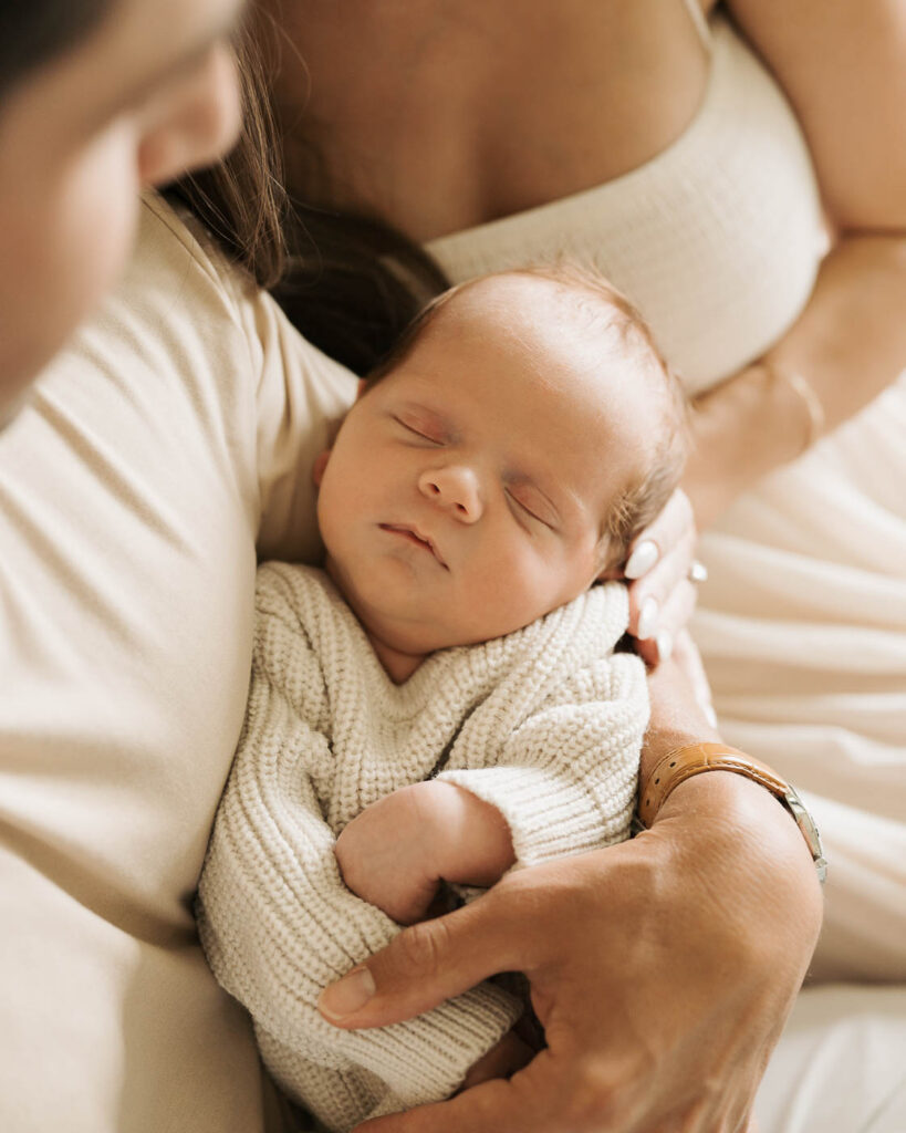 Mother Gently Cradling Her Sleeping Newborn Son In A Cream Knit Outfit During A Dallas Lifestyle Newborn Photography Session