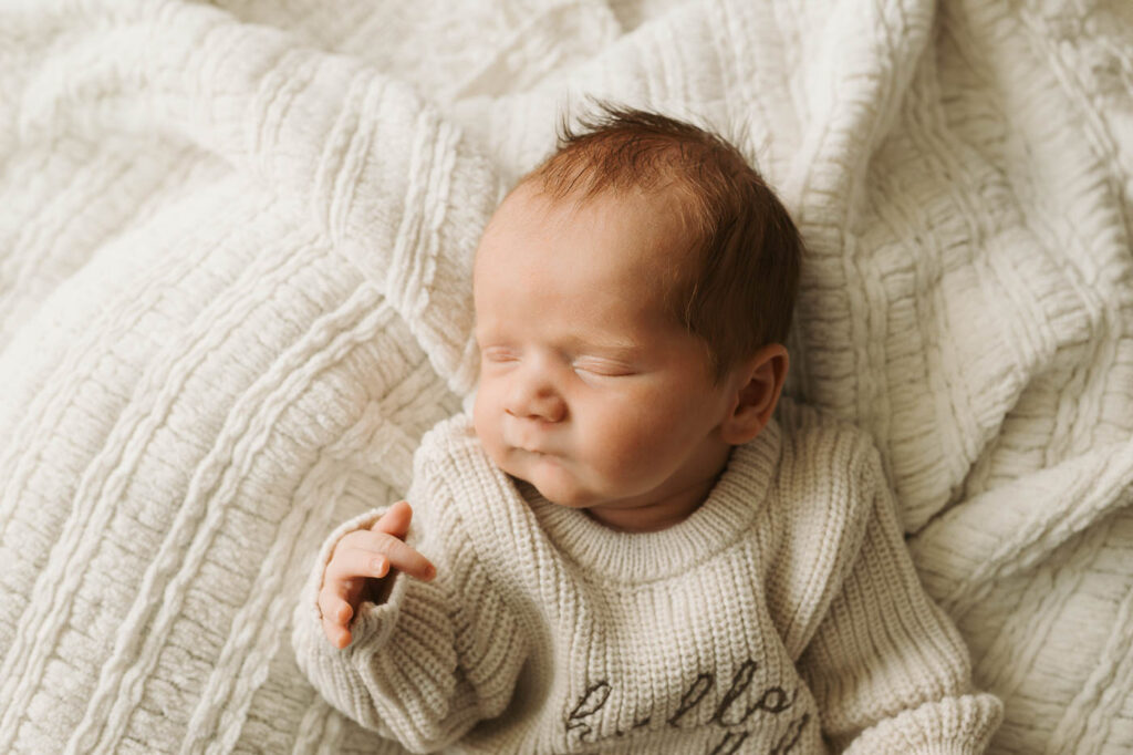 Sleeping Newborn Baby Boy Wearing A Cream Knit Outfit On An Ivory Textured Blanket During A Dallas Newborn Photoshoot
