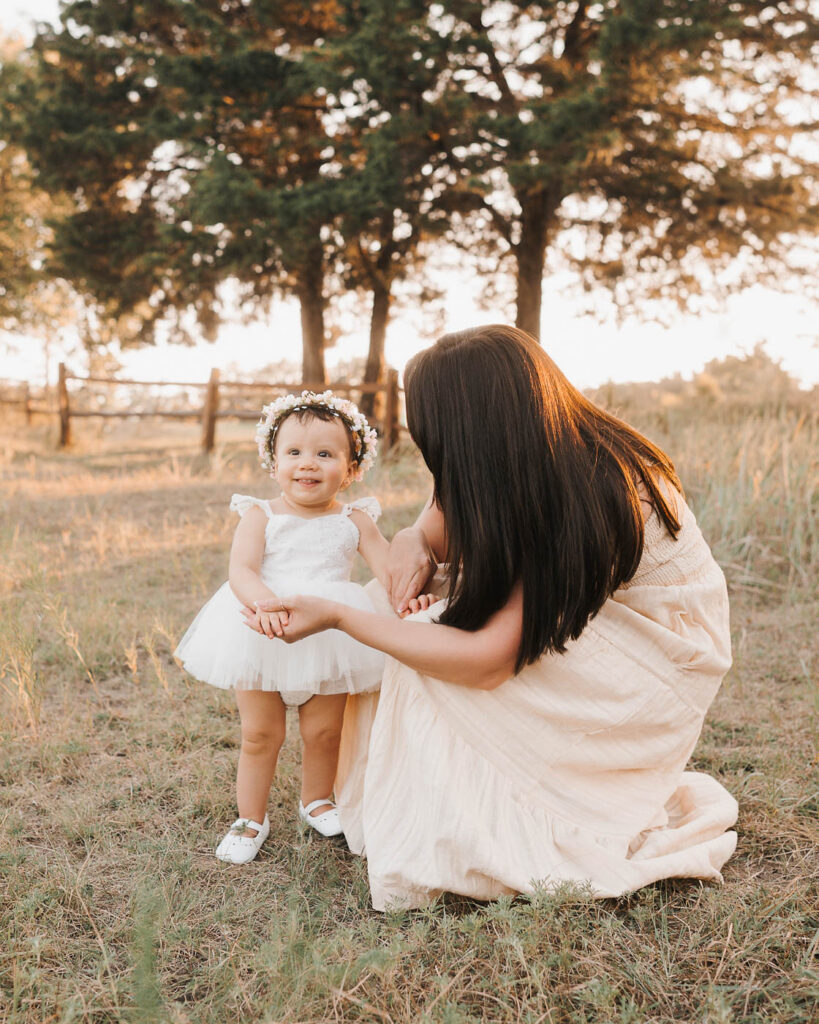 How I Create Natural Family Photos Without Awkward Posing 5 Mother Kneeling In A Grassy Field While Interacting With Her Toddler Daughter During A Candid Outdoor Family Photography Session.