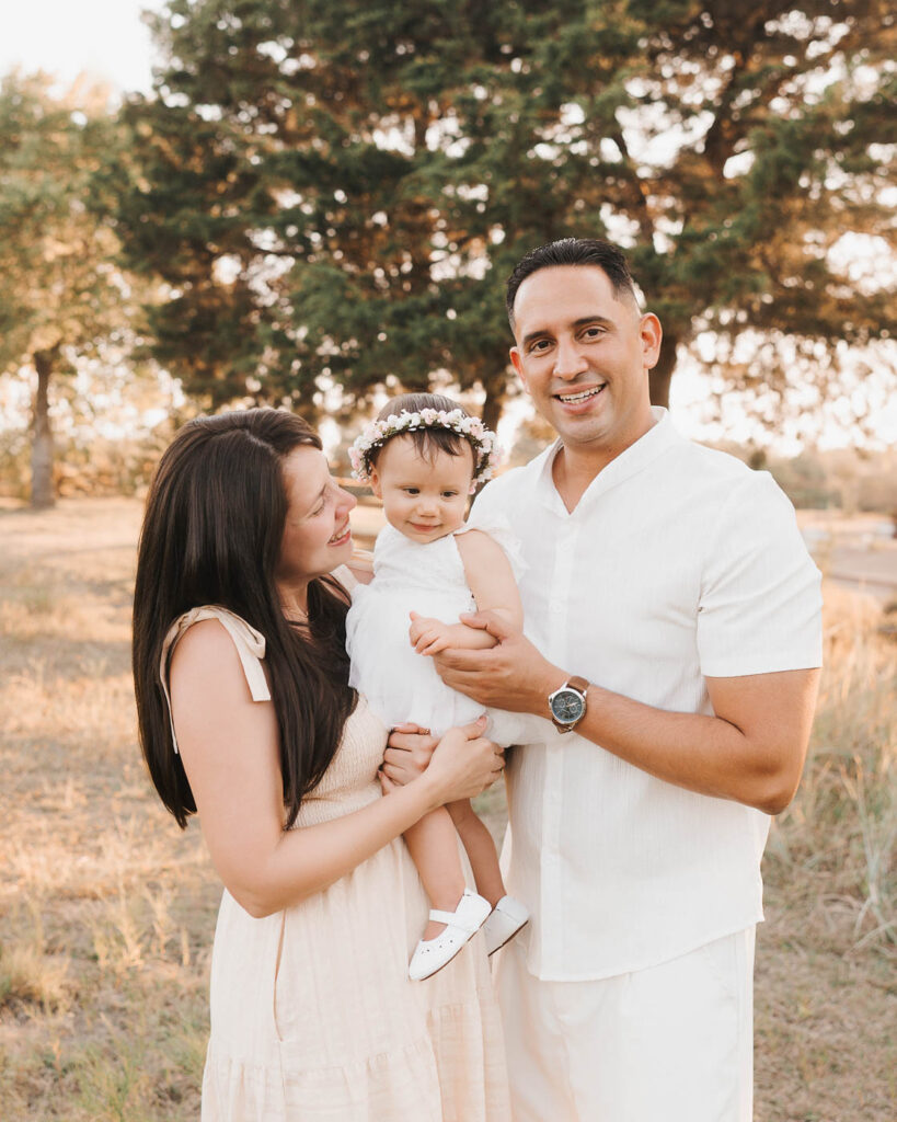 How I Create Natural Family Photos Without Awkward Posing 6 Dallas Family Photographer Capturing Parents Holding Their Smiling Toddler Daughter During A Golden-Hour Outdoor Family Session.