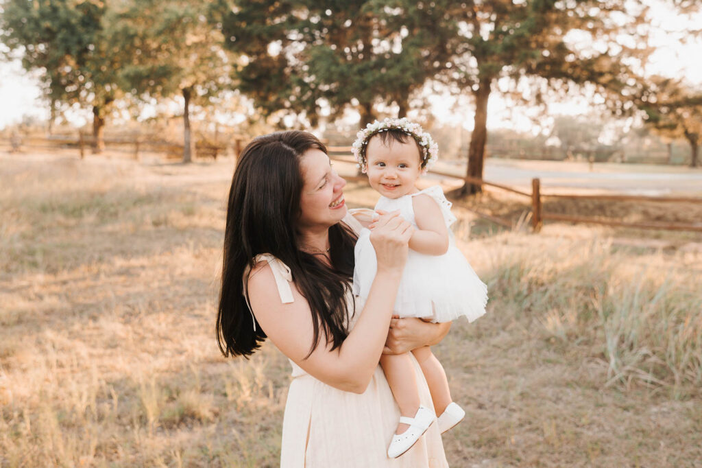 How I Create Natural Family Photos Without Awkward Posing 4 Mother Holding Her Smiling Toddler Daughter In A Sunlit Grassy Field During A Natural Family Photography Session In Dallas.