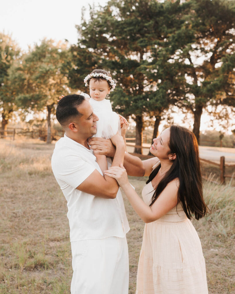 How I Create Natural Family Photos Without Awkward Posing 3 Parents Playfully Lifting Their Smiling Toddler Daughter During A Golden-Hour Outdoor Family Photography Session In Dallas.